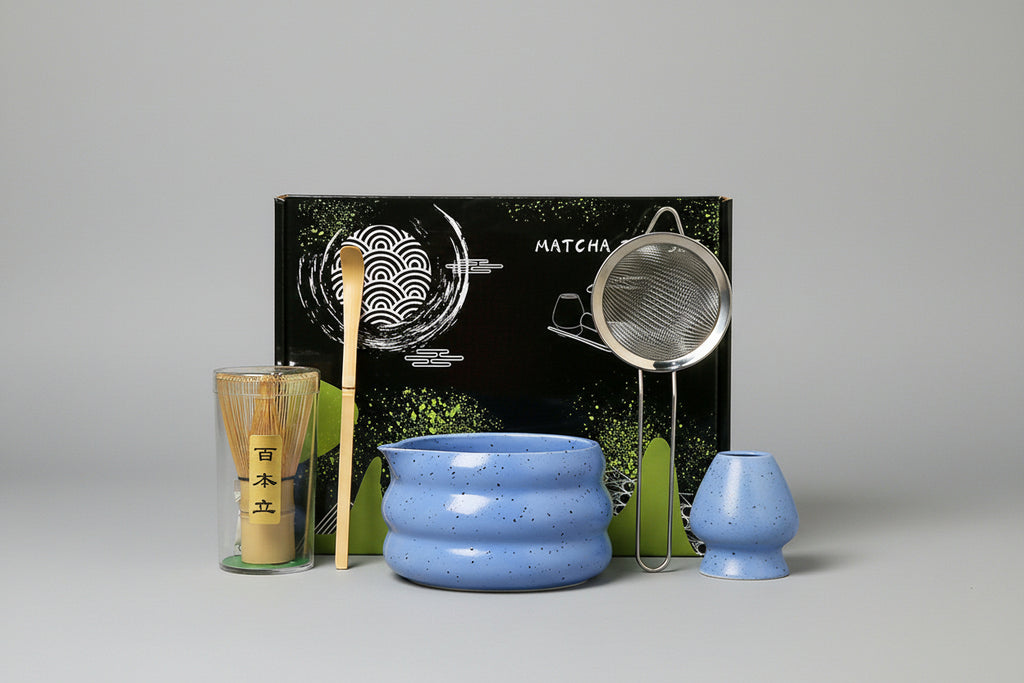 Matcha tea set with blue bowl, whisk, and other tools in front of a black box labeled 'Matcha'.